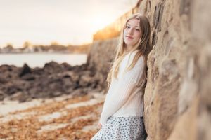 Casual portrait leaning against stone wall at sunset by the ocean.