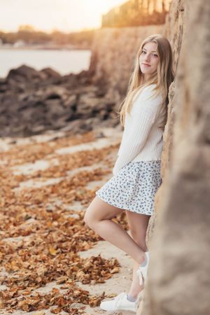 Outdoor fashion portrait at sunset wearing white sweater and floral skirt by rocky wall.
