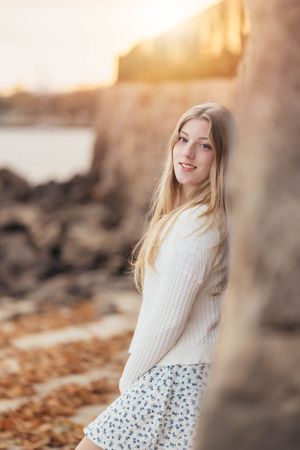 A golden hour portrait wearing white sweater and patterned skirt against rocky backdrop.