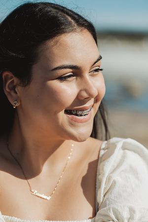 Close up portrait showing a bright smile with braces and delicate necklace in natural sunlight.