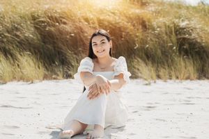 Person in flowing white dress poses on sandy beach during sunset.