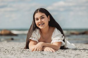 Person laying on beach sand with natural smile and long dark hair.