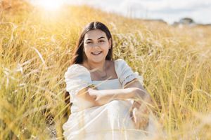 Person in white dress sitting in golden wheat field during sunset with warm lighting.