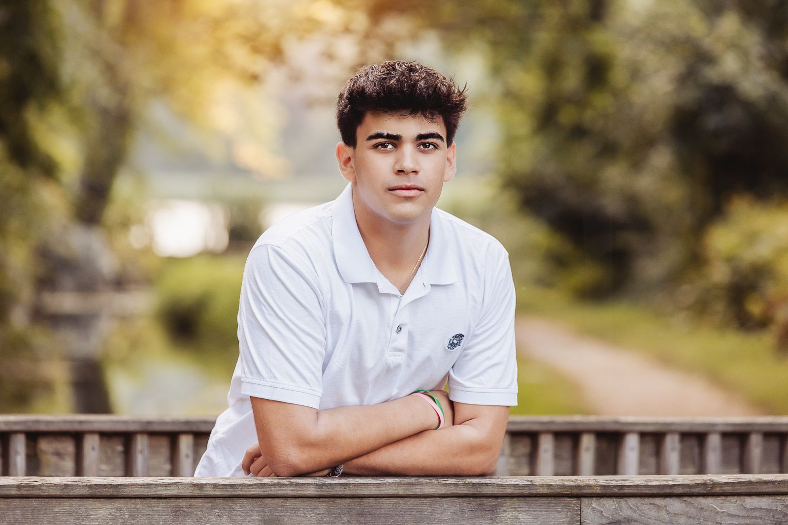 A young person in white polo leaning on wooden railing in autumn setting.