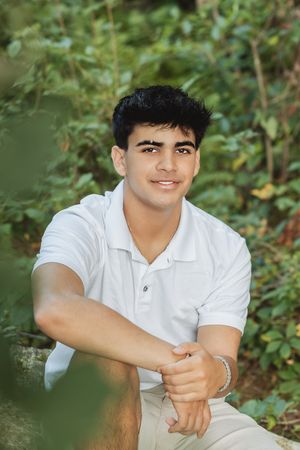 Person in white polo sitting outdoors with greenery and foliage in background.