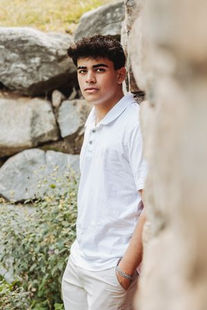 Person in white polo shirt leaning against rock wall in outdoor setting.