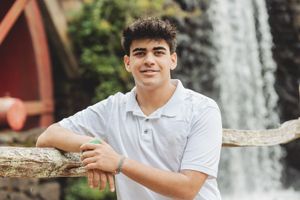 Person in white polo shirt poses by wooden railing with waterfall in background.