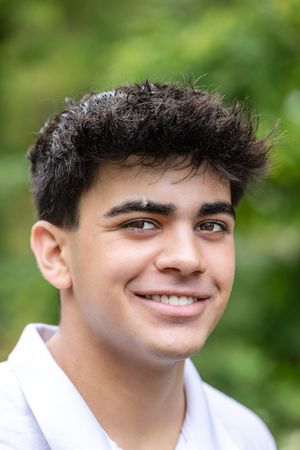 Portrait shot against blurred green background showing white polo shirt and natural lighting.