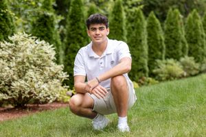 Person in white polo and shorts crouches on manicured lawn with landscaped garden background.