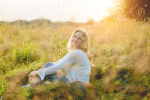 Woman relaxing in tall grass field during golden hour.