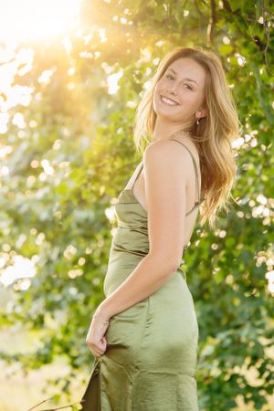 Woman in satin green dress posing outdoors with glowing sunset light.