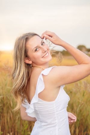 Candid portrait of woman in white dress enjoying a summer evening in a wheat field.