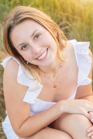 Portrait of woman in white ruffled dress smiling in sunlit field.