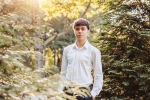 Portrait of person in white button-down shirt against natural forest background.