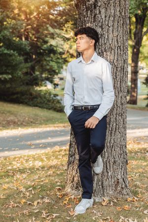 Person in white shirt and navy pants leaning against large tree trunk.