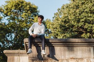 Person in casual attire sitting on stone wall overlooking sunny outdoor setting.