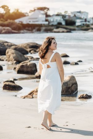 Beachside photo at sunset with white dress against rocky coastline.