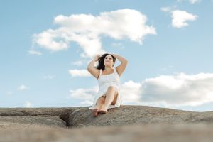 Relaxed summer portrait on rocky outcrop with cloudy blue sky backdrop.
