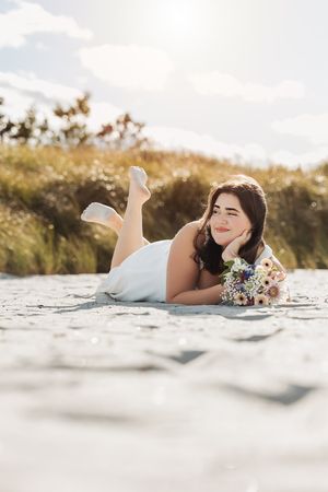 Dreamy portrait lying on rock with wildflower bouquet in golden sunlight.
