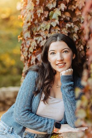 Autumn portrait with cozy blue sweater against colorful fall foliage background in warm golden light.