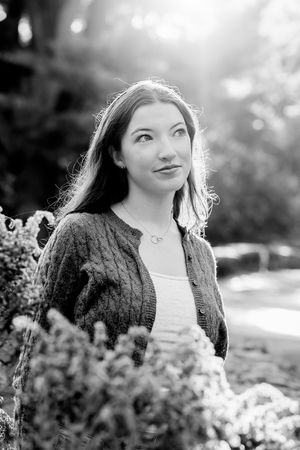 Black and white portrait series showing joyful expressions amid blooming flowers in a sunlit outdoor setting.