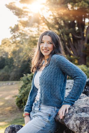 Outdoor portrait series in warm sunlight wearing a blue knit sweater and sitting on rocks.