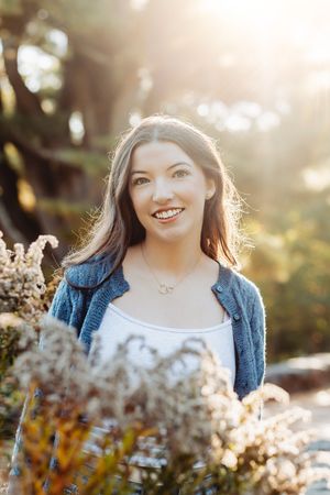 Outdoor portrait series in golden sunlight with dried flowers in foreground and denim jacket.