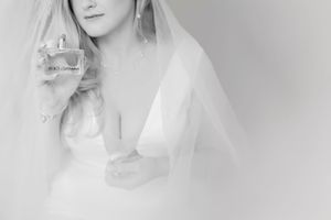 Black and white portrait of a bride in a deep-V wedding gown holding a Dolce & Gabbana perfume bottle.