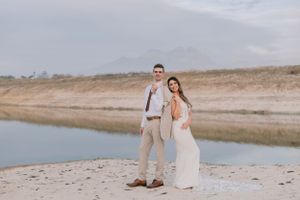 Bride and groom posing together in a scenic desert landscape with a serene lake and mountains in the background.