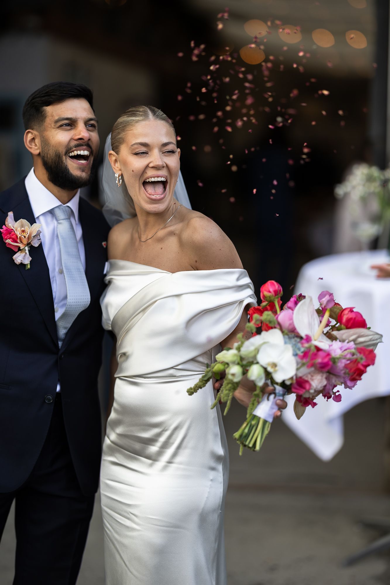 Happy newlyweds celebrate with pink flower petals falling around them during a joyful outdoor wedding celebration.