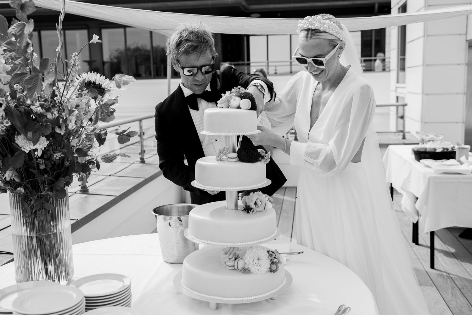 Black and white photo of wedding cake preparation at outdoor reception.