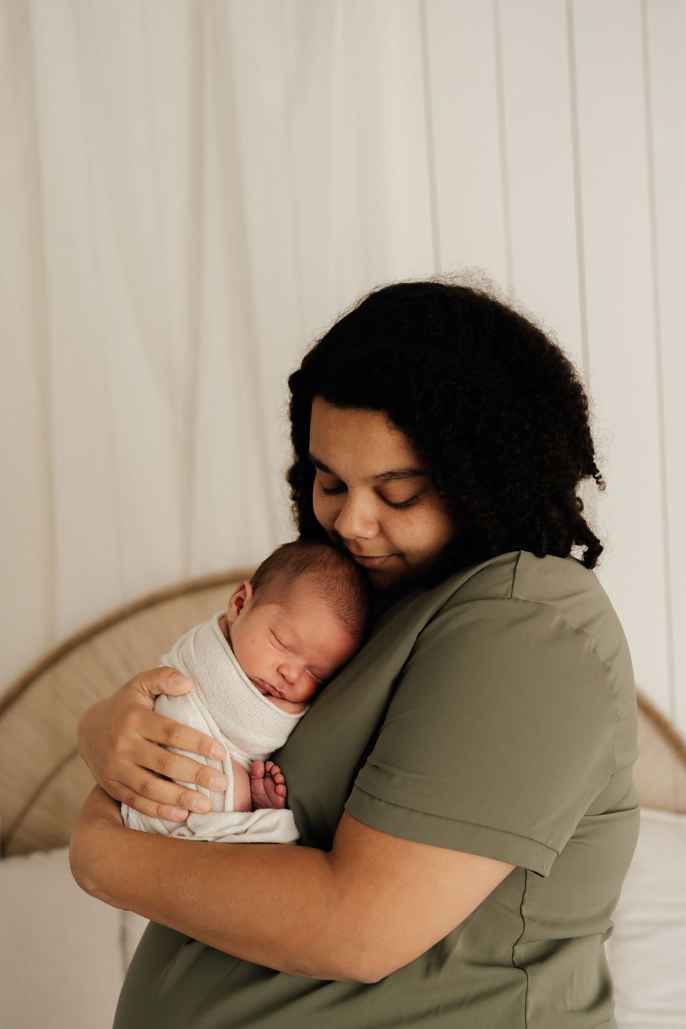 Tender moment captured as parent cradles sleeping newborn against olive green shirt.