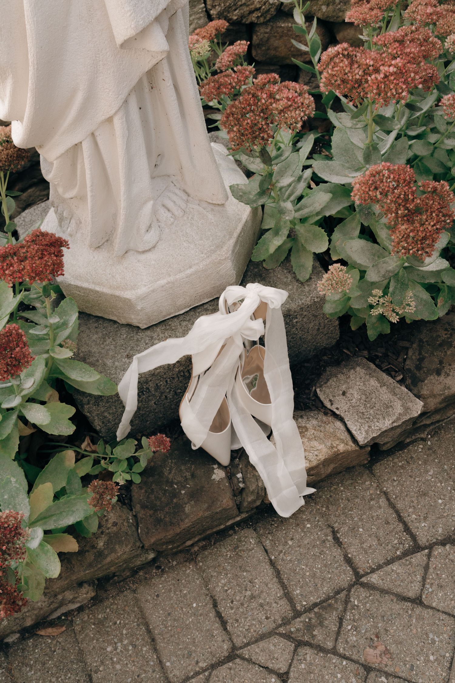 White fabric ribbons drape elegantly over stone steps alongside pink flowering plants and green foliage.