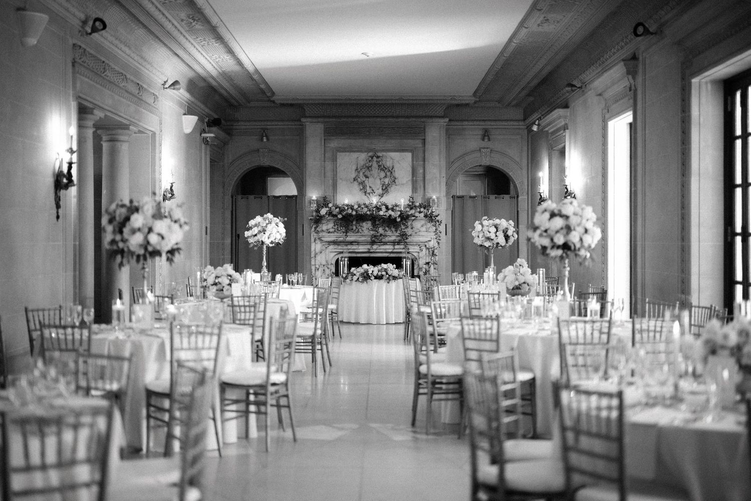 Elegant ballroom setup with white chairs and tables arranged for a formal wedding reception with crystal chandeliers.