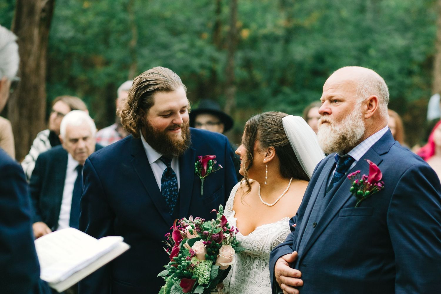 A group of wedding guests and attendees gather outdoors in formal attire during an elegant garden ceremony.