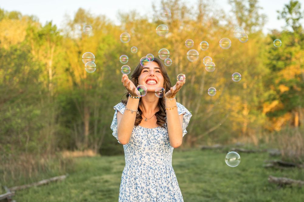 A woman in a floral dress plays with bubbles in a sunny field during golden hour.