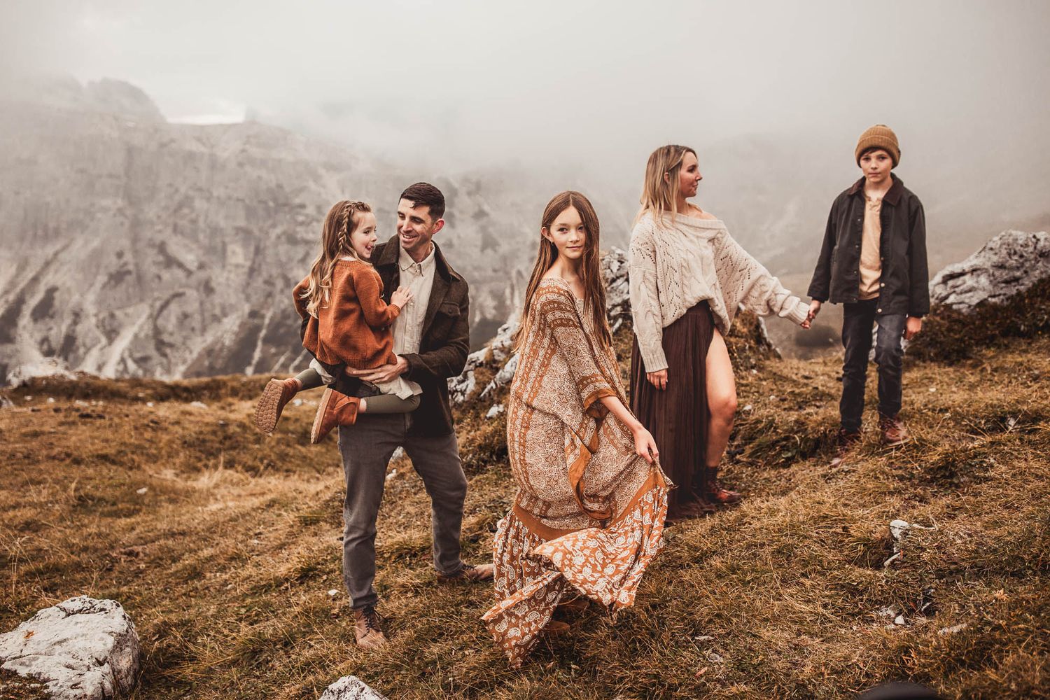 A group of people walk along a misty mountain ridge wearing boho style clothing in earth tones.