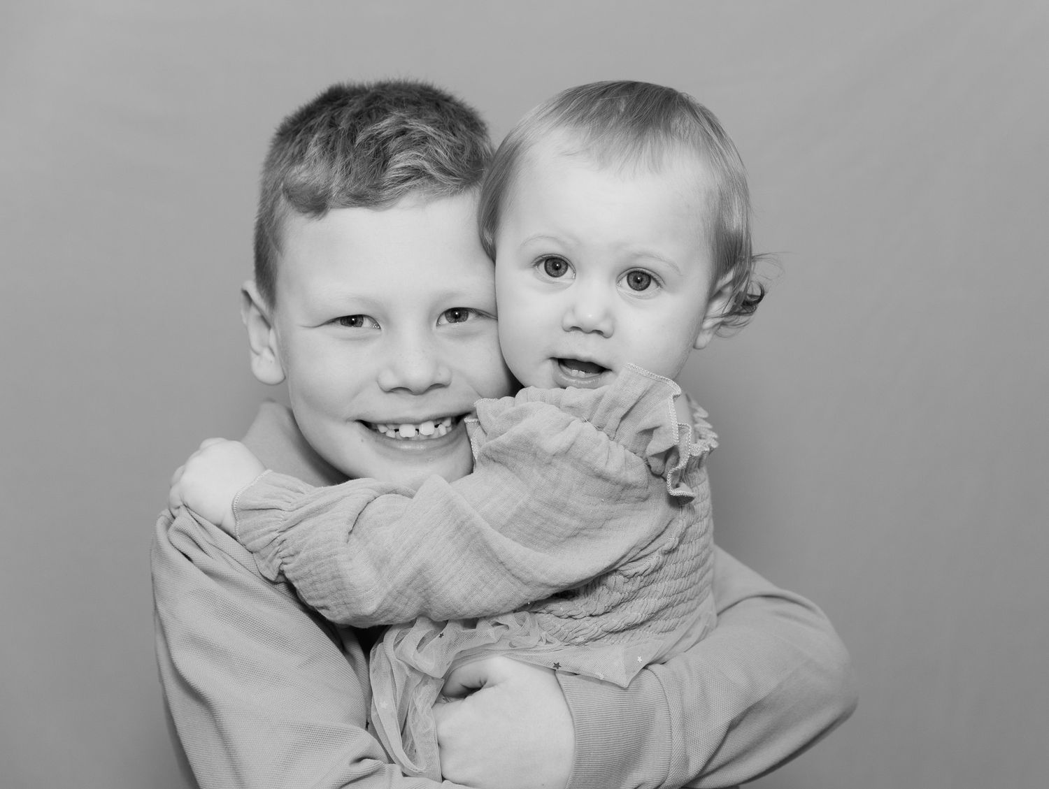 A black and white portrait of two siblings embracing, with one holding the other in a loving pose.