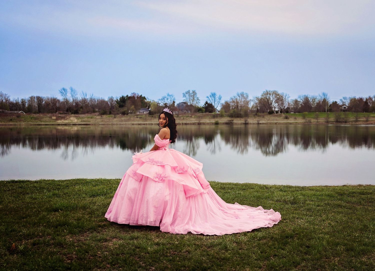A voluminous pink gown creates a striking silhouette against a lakeside landscape.
