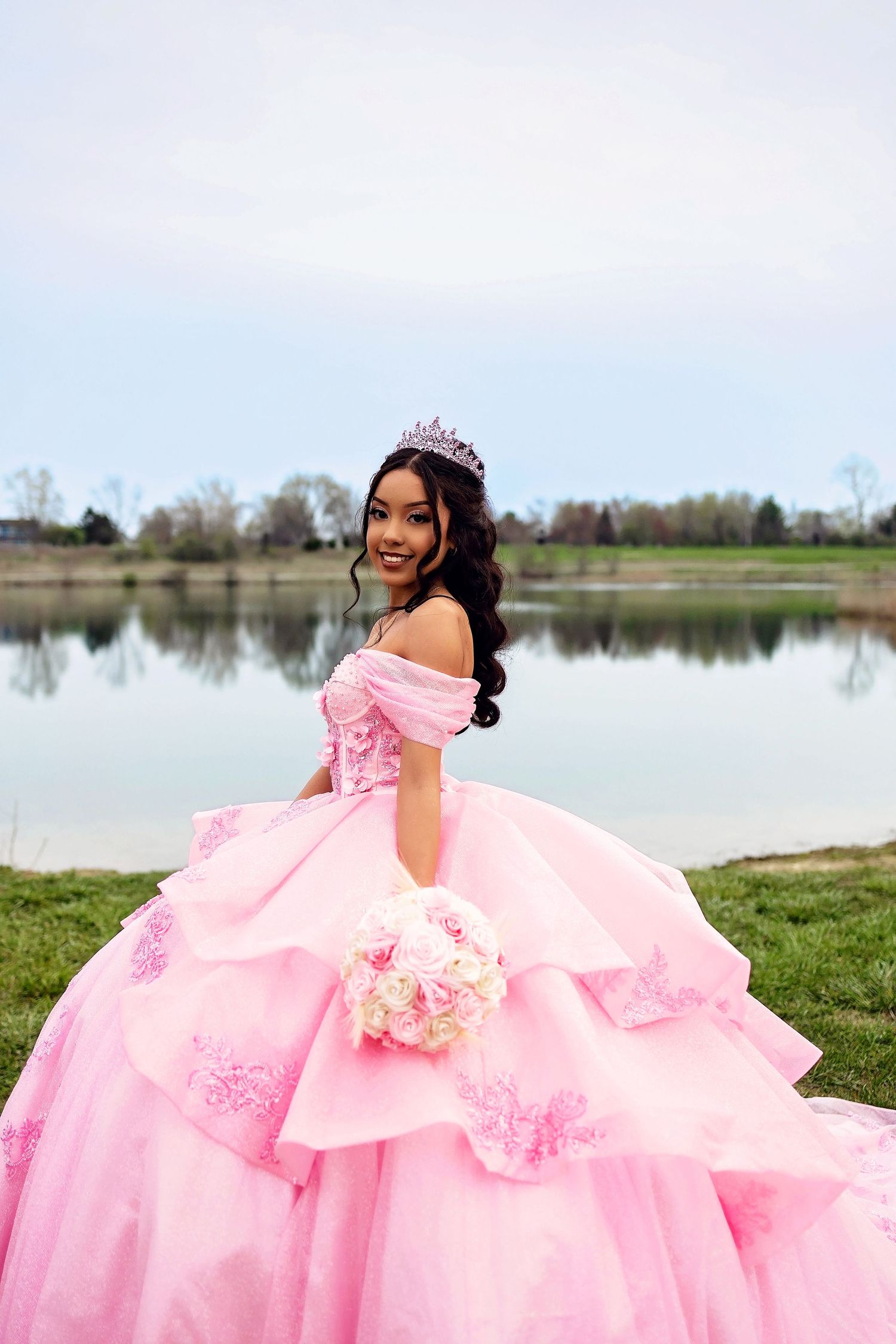 A dreamy pink ballgown sparkles in the sunlight by a reflective lake.