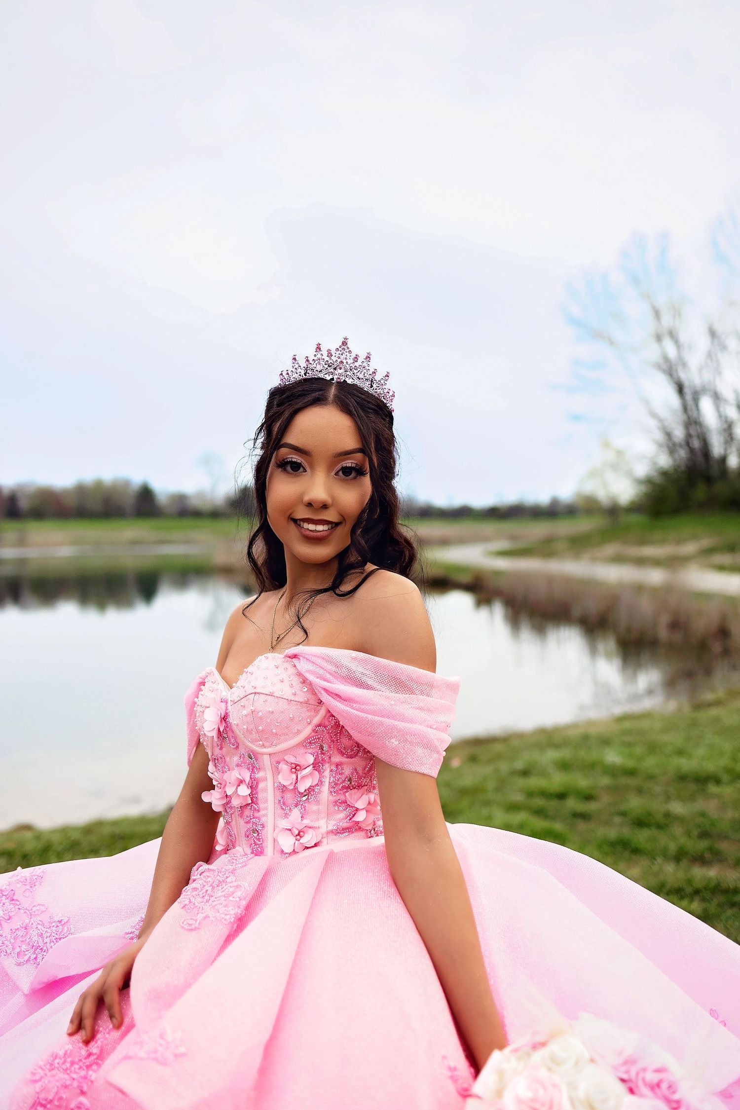 A glamorous pink princess dress with delicate details shimmers by a serene waterfront.