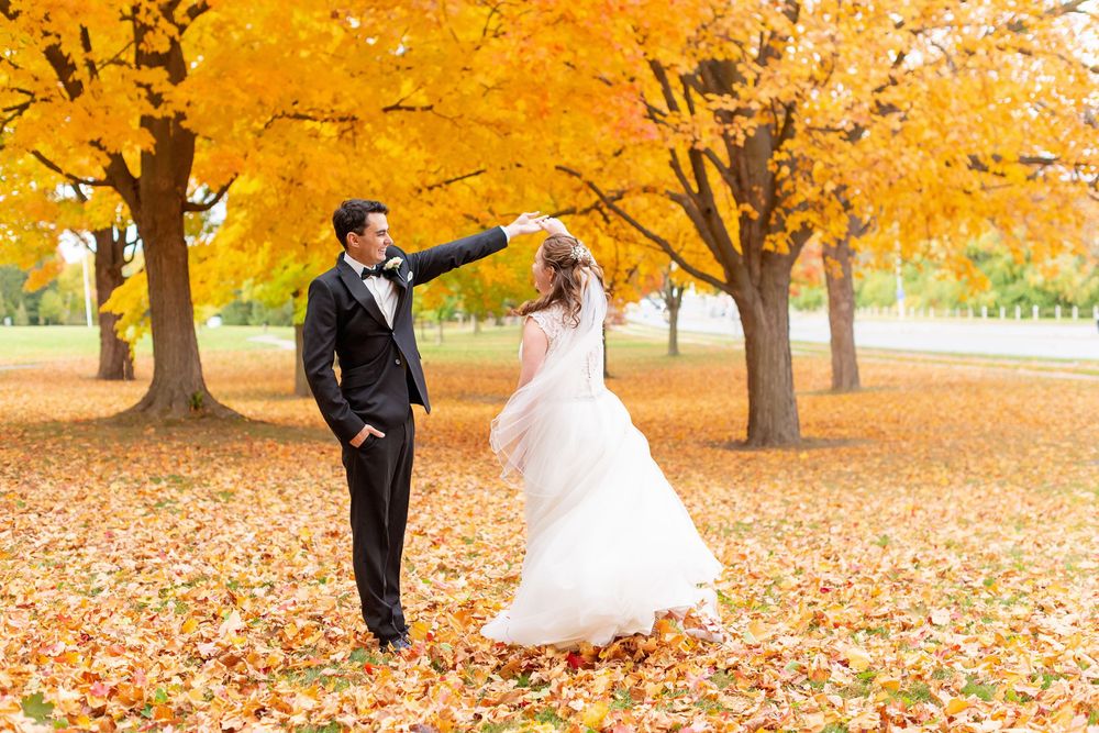 Couple dancing playfully in a park surrounded by vibrant yellow autumn leaves and trees.