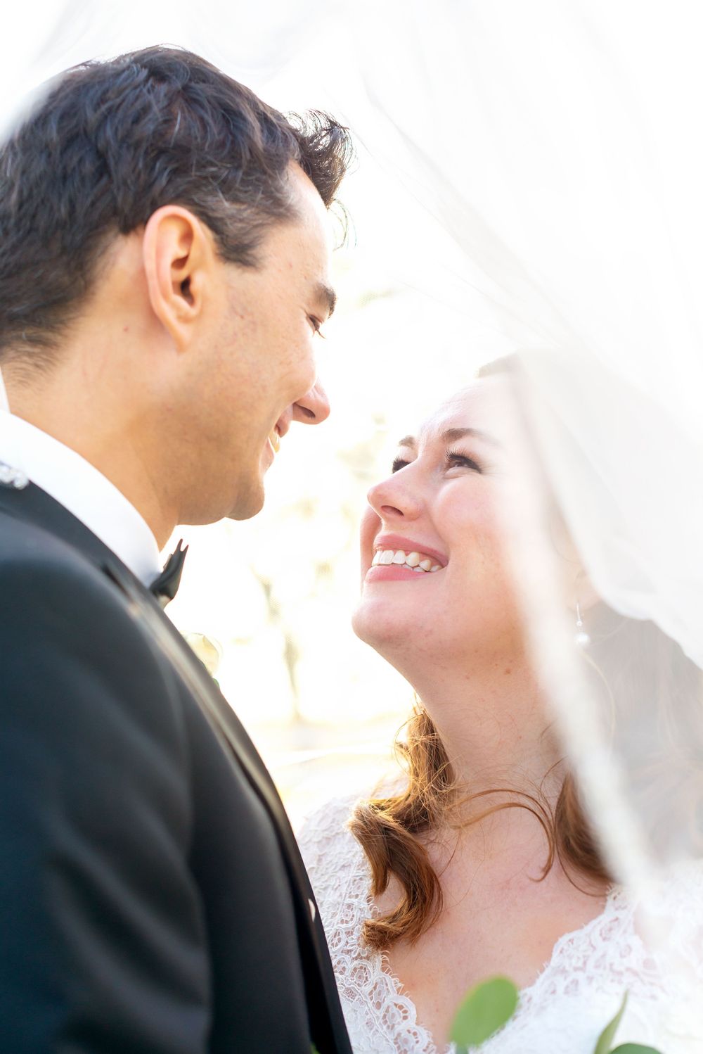 A joyful bride and groom share an intimate moment under her veil during their outdoor wedding ceremony.