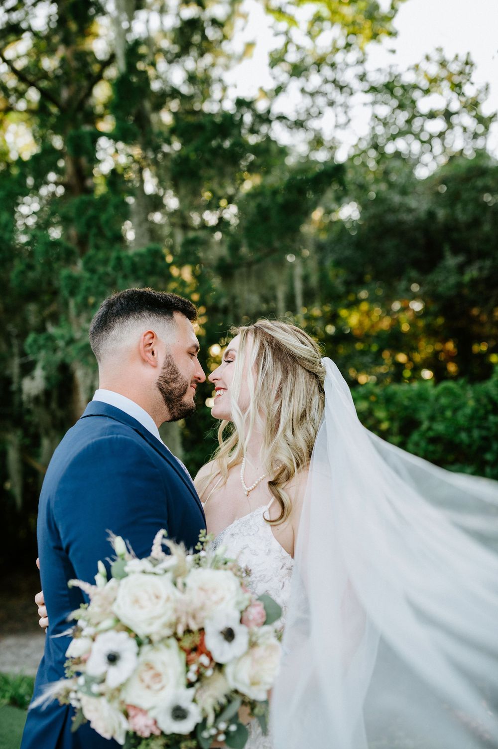 Newlywed couple shares romantic moments in a garden setting with flowing veil and white floral bouquet.