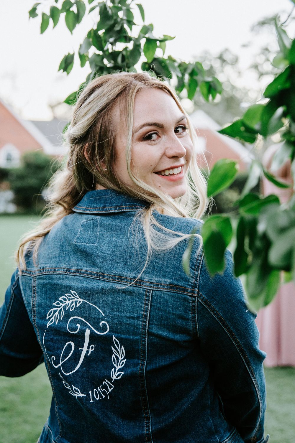 A denim jacket with custom white embroidered designs shown from multiple angles in an outdoor garden setting.