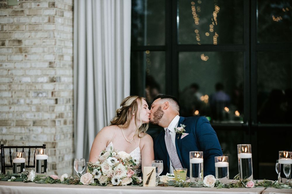 Elegant wedding reception table settings with white floral centerpieces and glowing candles in a rustic brick venue.