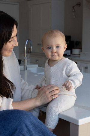 A smiling mother holds her blue-eyed baby on a kitchen counter, photographed during an in home session in Brighton