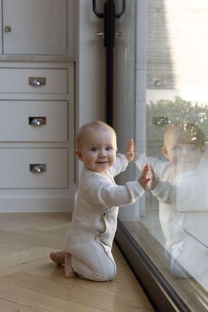 Baby leaning against window looking back at camera, taken during a family photography session in Brighton