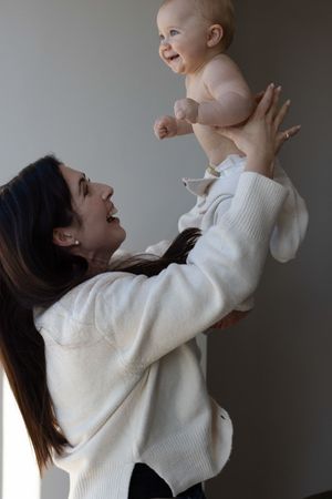 A smiling mother lifts her happy laughing baby overhead during a family photography session in Brighton