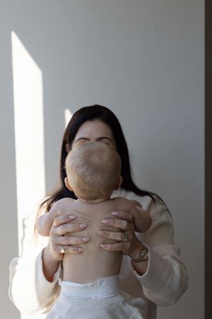 Mother lifting her baby up in a naturally lit room during an in home family portrait session in Brighton